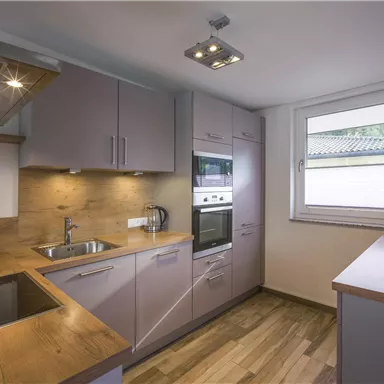 A modern kitchen with wooden surfaces and gray cabinets. Brightly lit room with windows and modern appliances.