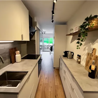 Eine moderne Küche mit hellen Schränken und einem großen Fenster. Der Raum ist gut beleuchtet und hat eine gemütliche Atmosphäre.