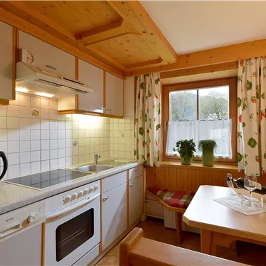 Eine gemütliche Küche mit Holzverkleidung und Geräten wie einem Herd und einer Kaffeemaschine. Am Fenster stehen Pflanzen, und ein Esstisch lädt zum Verweilen ein.