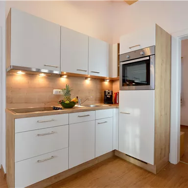 Eine moderne Küche mit weißen Möbeln und Holz-Details. Sie ist hell erleuchtet und gut ausgestattet.