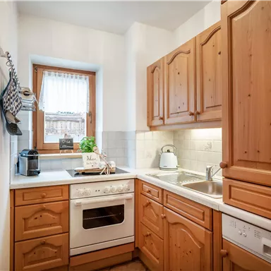 A cozy kitchen with wooden cabinets and modern equipment. A window provides daylight and a friendly atmosphere.