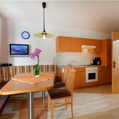 Küche mit Essbereich und holzfarbener Einrichtung. Ein Tisch mit Stühlen und eine Fensterbank mit Pflanzen sind sichtbar.