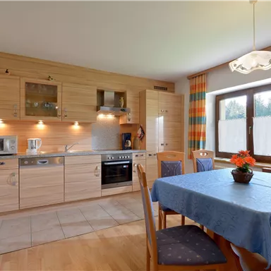 Eine moderne Küche mit Holzschränken und funktionaler Ausstattung. Der Tisch ist gedeckt und es gibt farbenfrohe Vorhänge am Fenster.