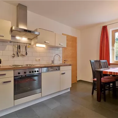 Eine moderne Küche mit einem Holzarbeitsplatz und weißen Schränken. Am Tisch stehen Stühle und es gibt ein Fenster mit Blick ins Grüne.