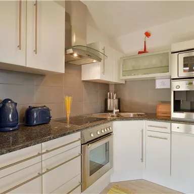 A modern kitchen with white cabinets and a black countertop. There are various kitchen appliances, including a stove, a microwave, and a kettle.