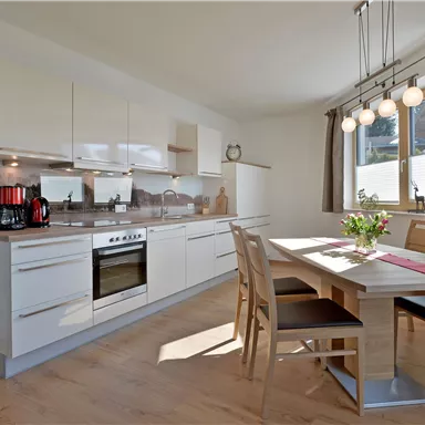 Eine moderne Küche mit hellen Möbeln und viel natürlichem Licht. Der Esstisch ist liebevoll gedeckt und bietet Platz für mehrere Personen.