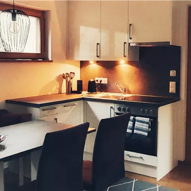 A modern kitchen with a table and black chairs. The furniture is bright and the room is well lit.