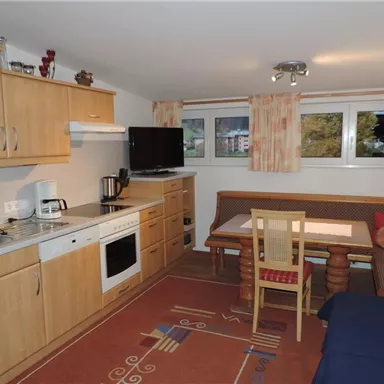 Eine gemütliche Küchenzeile mit Holzschränken und modernen Geräten. Ein Essbereich mit einem Tisch und einer Eckbank lädt zum Verweilen ein.