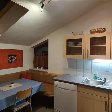 A cozy kitchen with a dining table and a seating area. Photos hang on the wall, and the light is friendly and inviting.