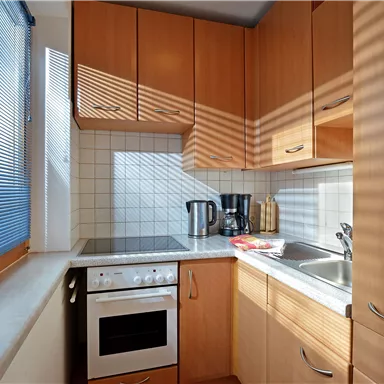 Eine moderne Küche mit Holzschränken und weißen Fliesen. Die Sonne scheint durch das Fenster und wirft Schatten auf die Arbeitsfläche.