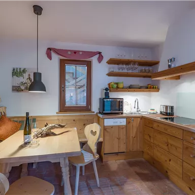 A cozy kitchen with wooden paneling and modern fixtures. A dining table with chairs and a window that provides daylight.