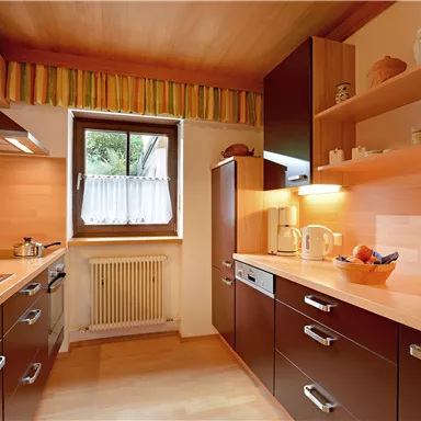 Eine moderne Küche mit Holzregalen und dunklen Schrankfronten. Sie ist hell beleuchtet und verfügt über eine große Fensterfront.