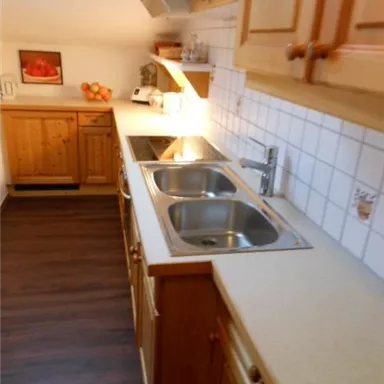Eine gemütliche Küche mit Holzschränken und einem Doppelspülbecken. Die Arbeitsfläche ist hell und es gibt eine angenehme Beleuchtung.