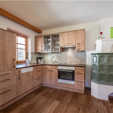 A modern kitchen with wooden furniture and a bright, open space. The amenities include a stove, a refrigerator, and a cozy seating area.