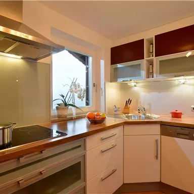 Eine moderne Küche mit Holzarbeitsfläche und eleganten Schränken. Der Raum ist gut beleuchtet und enthält Küchenutensilien sowie frisches Obst.