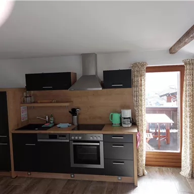 Eine moderne Küche mit Holz- und schwarzen Elementen. Fenster mit Vorhängen bieten Blick nach draußen.