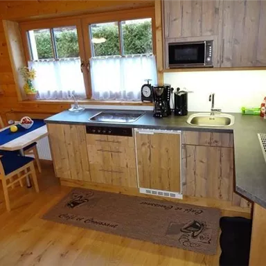 Eine moderne Küche aus Holz mit einem Herd, Mikrowelle und Spüle. Es gibt einen kleinen Tisch mit Stühlen und viel Tageslicht durch die Fenster.