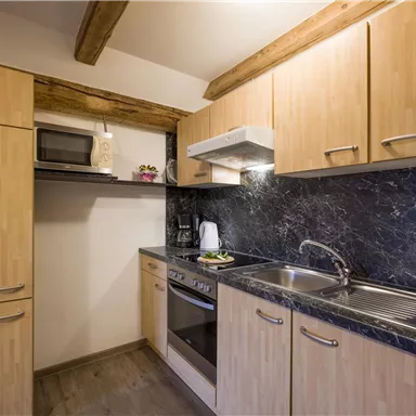 Eine moderne Küche mit Holzschränken und einer dunklen Arbeitsplatte. Sie ist ausgestattet mit einem Kühlschrank, einer Mikrowelle und einem Herd.