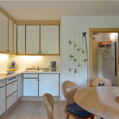 A cozy kitchen with modern appliances and a wooden dining table. The walls are bright and decorated with plants.