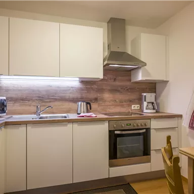 A modern kitchen with bright cabinets and wooden details. Fresh fruit is on the table, and there is a microwave and a coffee machine.
