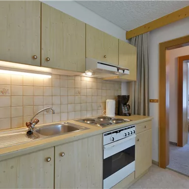 Eine moderne Kücheneinheit mit Holzschränken und einem Herd. Im Hintergrund sieht man einen Zugang zu einem weiteren Raum.