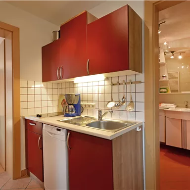 Eine moderne Küche mit roten Schränken und einer Spüle. Im Hintergrund ist ein Badezimmer zu sehen.
