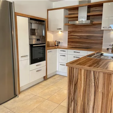 Moderne Küche mit weißen Schränken und einer Holzarbeitsplatte. Am linken Rand steht ein Kühlschrank aus Edelstahl.