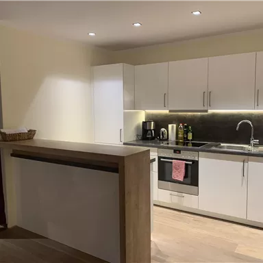 Eine moderne Küche mit weißen Schränken und einer stilvollen Arbeitsfläche. Die Ausstattung umfasst einen Herd, eine Spüle und verschiedene Haushaltsgeräte.