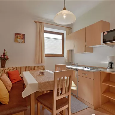 Eine gemütliche Küche mit einem Esstisch und einer kleinen Sitzbank. Die Einrichtung ist hell und modern mit verschiedenen Küchenutensilien.