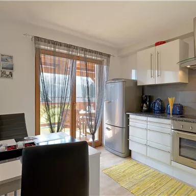 A modern kitchen with a refrigerator, a stove, and a dining area.  
Large windows let in plenty of light and offer a view of the outdoor area.
