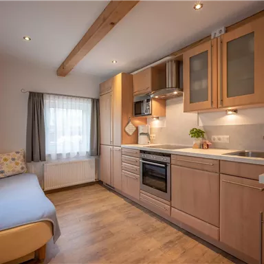 Eine moderne Küche mit Holzschränken und hellem Holzfußboden. Die Fenster lassen viel Tageslicht herein.