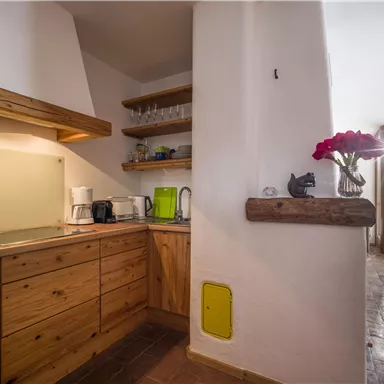 A modern kitchen with wooden shelves and sleek appliances. Large windows let in plenty of light and provide a view of the surroundings.