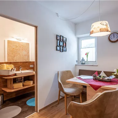 A cozy dining area with a table and chairs. In the background, a bathroom is visible, which is modernly furnished.