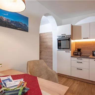 A modern kitchen with a table and chairs. In the background, mountain landscapes can be seen on the wall.