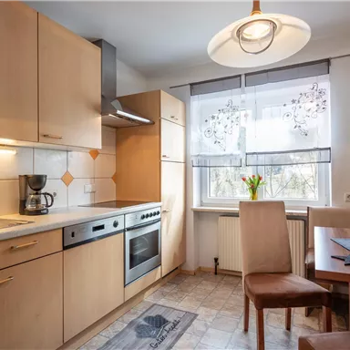 A modern kitchen with wood cabinets and a bright table. On the table, there are fresh flowers and a coffee pot.
