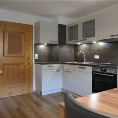 Eine moderne Küchenzeile mit weißen Möbeln und Holzdetails. Die Küche ist gut beleuchtet und wirkt einladend.