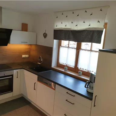 Eine moderne Küche mit weißen Schränken und Holzdetails. Sie verfügt über eine Edelstahl-Spüle und große Fenster, die viel Licht hereinlassen.