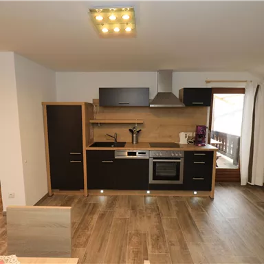 Eine moderne Küche mit Holzfußboden und eleganten schwarzen Schränken. Das Fenster bietet Blick auf einen Balkon.