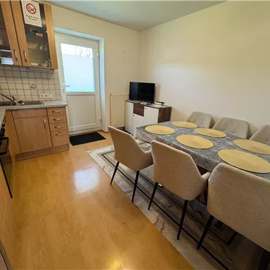 Eine moderne Küche mit einem Essbereich. Der Tisch ist gedeckt und es gibt einen Fernseher sowie eine Tür, die nach draußen führt.