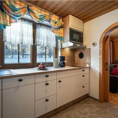 Eine moderne Küche mit hellen Möbeln und großen Fenstern. Durch die Fenster ist ein winterlicher Ausblick zu sehen.