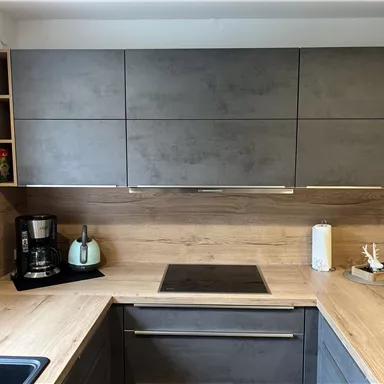 Moderne Küche mit Holzoberflächen und grauen Schränken. Auf der Arbeitsplatte stehen eine Kaffeemaschine und ein Wasserkessel.