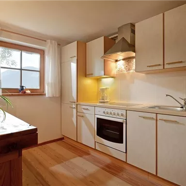 A bright and modern kitchen with wooden details. The furnishings include a stove, a refrigerator, and a sink, with a window that lets in daylight.