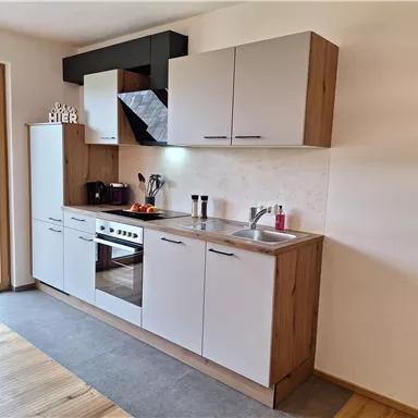 Eine moderne Küche mit hellen Schränken und einer Kochzeile. Der Raum hat große Fenster, die viel Tageslicht hereinlassen.