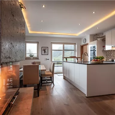 Eine moderne Küche mit einem großen Küchenblock und einem offenen Essbereich. Ein Kamin sorgt für eine gemütliche Atmosphäre.