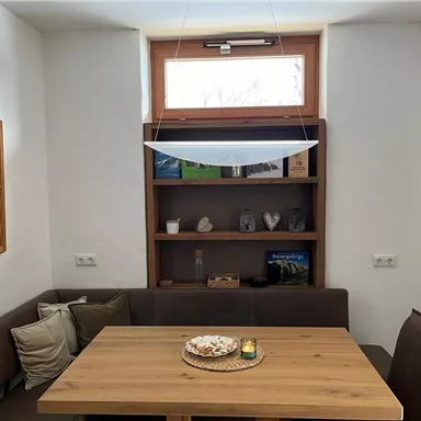 Ein gemütlicher Essbereich mit einem Holztisch und einer Bank. An der Wand hängen Bilder, und im Regal sind dekorative Gegenstände platziert.