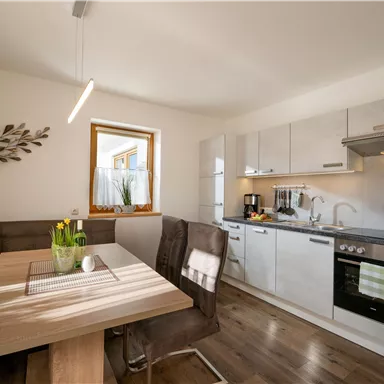 A modern kitchen with a wooden farmhouse table and cozy chairs. Bright, neutral colors and a window create an inviting atmosphere.
