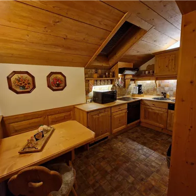 Eine gemütliche Küche im Landhausstil mit Holzvertäfelung und einem Tisch. Die Ausstattung umfasst einen Herd, eine Mikrowelle und dekorative Wandbilder.