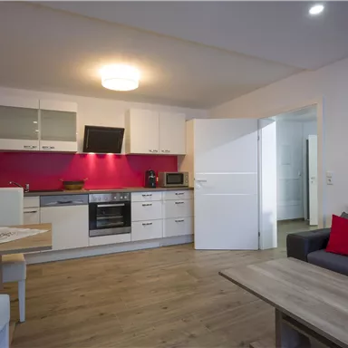 Modern kitchen with white furniture and a red accent wall. The space is bright and inviting.