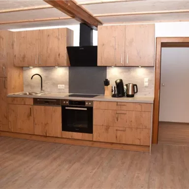 A modern kitchen with wooden furniture and a clear countertop. The room is bright and inviting with a dining area and a sofa.