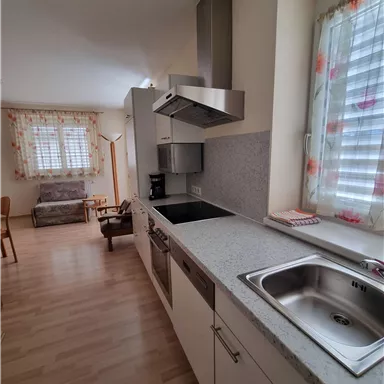 Eine moderne Küche mit hellen Möbeln und einem Fenster mit Vorhängen. Der Raum ist gut beleuchtet und offen gestaltet.